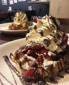 a waffle topped with whipped cream and strawberries sits on a plate next to other desserts