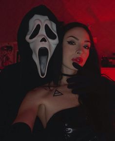 a woman wearing a ghost mask and black latex with her hand on her chest