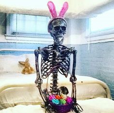 a skeleton sitting on top of a bed with an easter basket in front of it