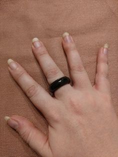 a woman's hand with a black ring on top of her left hand, resting against a tan cloth