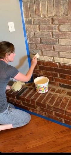 a woman sitting on the floor painting a brick fireplace