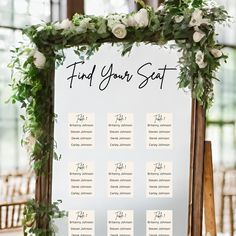 a seating chart with white flowers and greenery on the table for a wedding ceremony