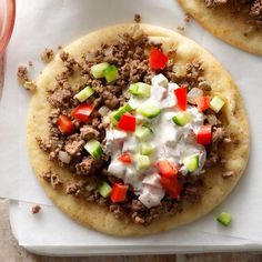 two pita breads topped with meat, vegetables and yogurt on a cutting board