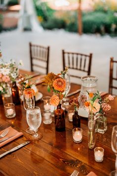 a wooden table topped with lots of vases filled with different types of flowers and candles