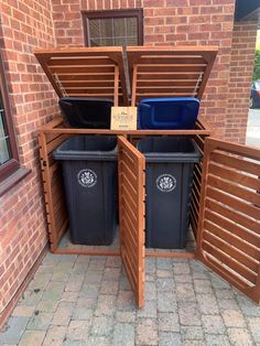 three trash cans are in the corner of a wooden fenced area with two bins on each side