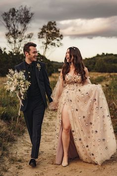 a man and woman walking down a dirt road holding each other's hands as they walk towards the camera