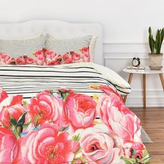 a bed with pink roses on it in a room next to a potted plant