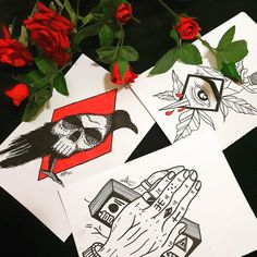 three cards with different designs on them sitting next to red roses and one has a bird