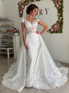 a woman in a white wedding dress standing next to a wall with flowers on it