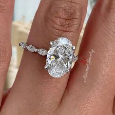 a woman's hand with a diamond engagement ring on her left hand and an oval shaped