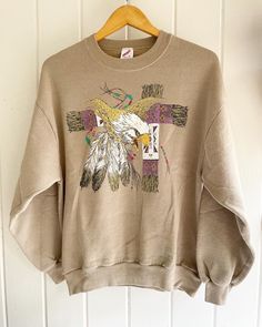 Vintage Native American Feathers Eagle Beads Graphic Tee T Shirt L Made in USA. XCIII Wildside. Sparkle gold. Some cracking in the white (see all pictures.) Beige cotton/Poly sweatshirt. Size: L. Length: 27" Underarm to Underarm: 22.5" . Orders over $35 ship for free. Please check out my Instagram for my newest finds: Hollyshopvintage  Everything priced over $35 has shipping already included in the total price. I'll gladly combine shipping on multiple items to save you money, when it is safe to do so! Message me to make adjustments ahead of time, or make your purchase and I'll refund the shipping overages.  Most items are Vintage. Expect some vintage wear. Items may contain unmentioned flaws.  I only post items that have a lot of life left. I do my best to accurately describe each item. Pl Vintage Gold Tops With Graphic Print, Vintage Gold Top With Graphic Print, Gold Vintage Tops With Graphic Print, Vintage Gold Crew Neck Top, Gold Crew Neck T-shirt For Fall, Modern Native American Fashion, Native American Feathers, New Braunfels, Native American Fashion