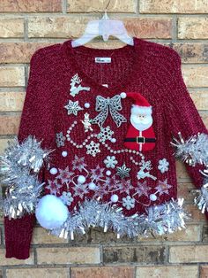 a red sweater with silver snowflakes and santa clause on it, hanging against a brick wall