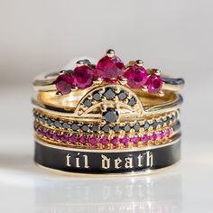 a stack of rings with pink and black stones on each one, sitting on a white surface