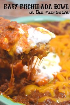 a spoon full of chili and cheese being lifted from a casserole dish with text overlay that reads easy enchilada bowl in the microwave