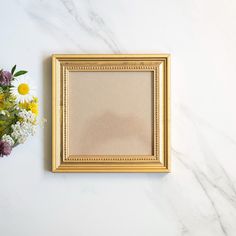 a gold frame sitting on top of a white marble counter next to a bouquet of flowers