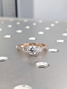 an engagement ring with three stones on it sitting on top of a metal table surrounded by silver circles