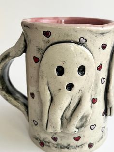 a ceramic cup with two faces and hearts on the inside is holding an elephant's trunk