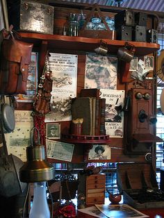 an old fashioned desk with lots of items on the shelves and around it is a clock