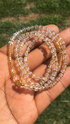 a hand holding a beaded bracelet in it's left hand, with grass in the background