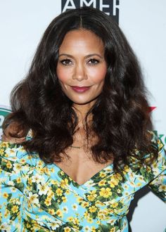 a woman with long dark hair wearing a blue floral dress and smiling at the camera