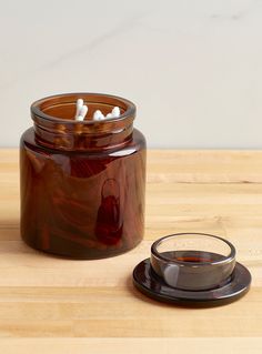 a glass jar filled with liquid sitting on top of a wooden table next to a cup