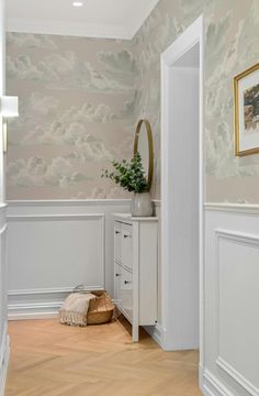 a white cabinet sitting in the middle of a living room next to a wall with clouds painted on it