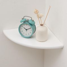 a blue alarm clock sitting on top of a white shelf next to a vase with flowers