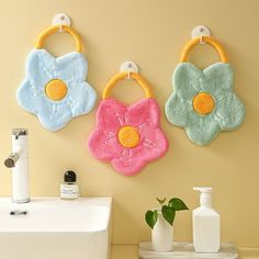 three flower shaped towels hanging on the wall next to a white sink and soap dispenser