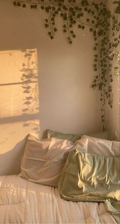 an unmade bed with white sheets and plants growing on the wall above it, in front of a window