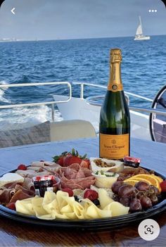 a bottle of champagne and some food on a table near the ocean with a boat in the background