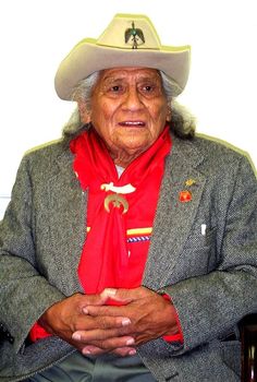 an old man wearing a cowboy hat and red scarf with his hands folded in front of him