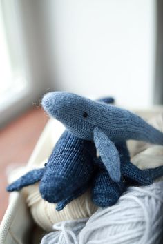 two blue knitted dolphins sitting on top of balls of yarn in a basket next to a window