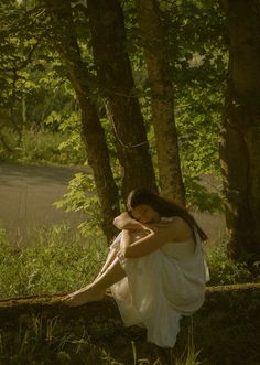 a woman sitting in the grass next to some trees