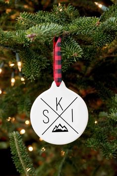 a white ornament hanging from a christmas tree with red and black plaid ribbon