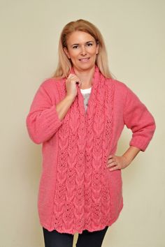 a woman wearing a pink cabled sweater and black leggings stands in front of a white wall