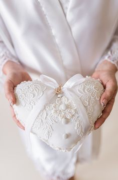 a woman holding a white heart shaped pillow in her hands with a wedding ring on it