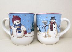 two coffee mugs decorated with snowmen on the front and back, one has a blue background