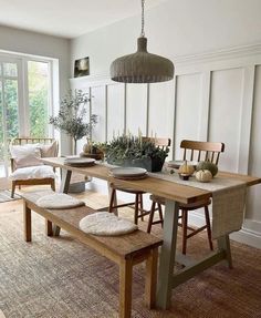 a dining room table with two benches in front of it and potted plants on the other side