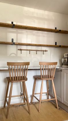 two wooden bar stools sitting next to each other in a kitchen with white walls