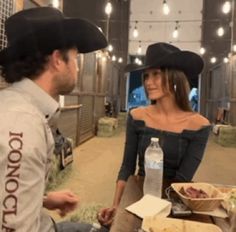 a man and woman sitting at a table with food in front of them, talking to each other