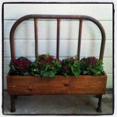 a wooden bench with plants in it sitting on the ground next to a white wall