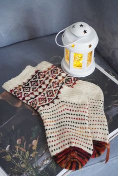 a white lantern and some knitted items on top of a magazine with an image of a woman's sweater