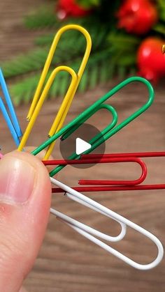 a hand holding several colored paper clips on top of a wooden table next to christmas decorations