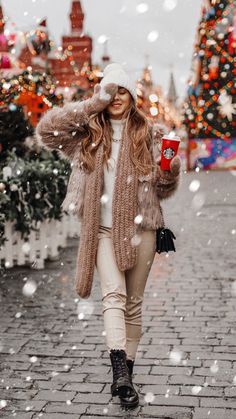 a woman is walking down the street with her coffee in hand and snow falling around her