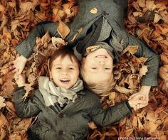 two young children laying in leaves on the ground with their faces close to each other