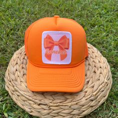 an orange trucker hat with a bow on it sitting in the middle of some grass