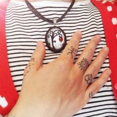 a woman wearing a red and white striped shirt with tattoos on her hand, holding onto a black pendant