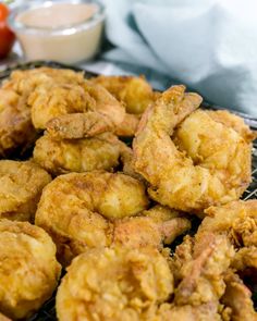 fried food sitting on top of a metal rack next to tomatoes and sauces in bowls