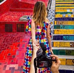 a woman in a colorful dress walking up some stairs with a camera on her hand