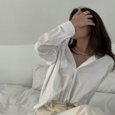 a woman sitting on top of a bed holding her hand up to her face and covering her eyes